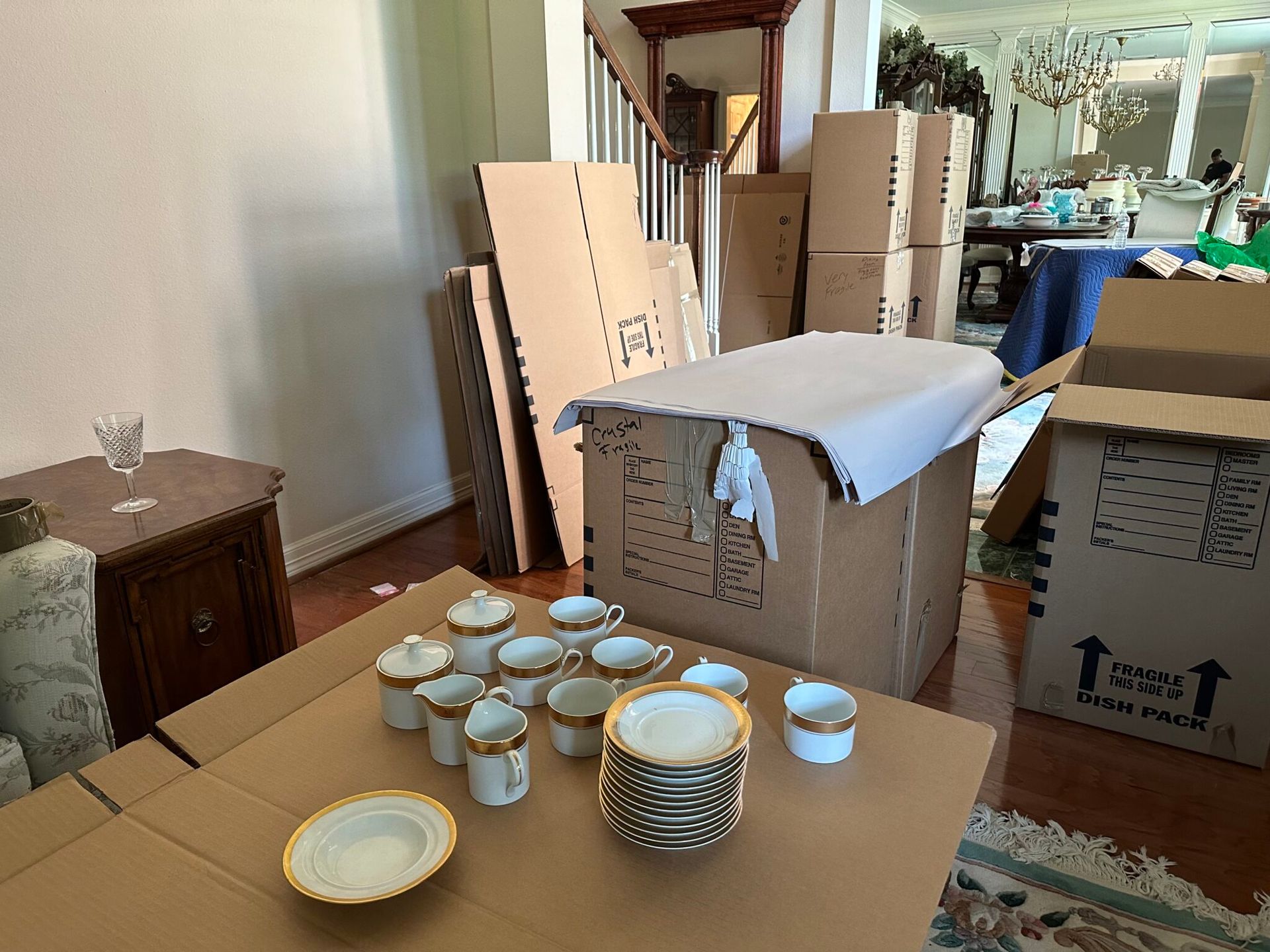 A table with plates , cups and saucers on it surrounded by cardboard boxes.