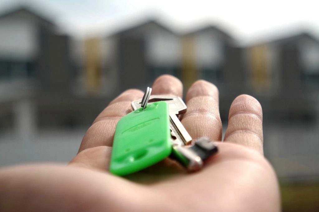 A hand holding a set of house keys on a green key tag