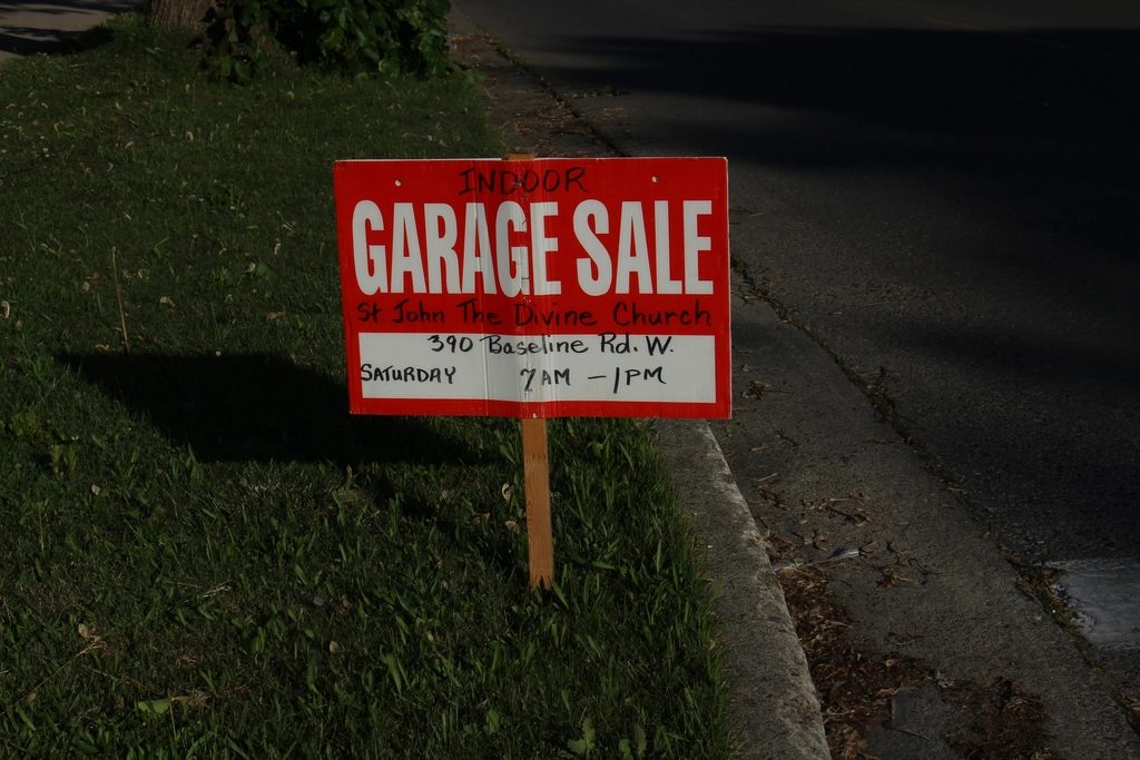 A handwritten garage sale sign on a lawn beside the street