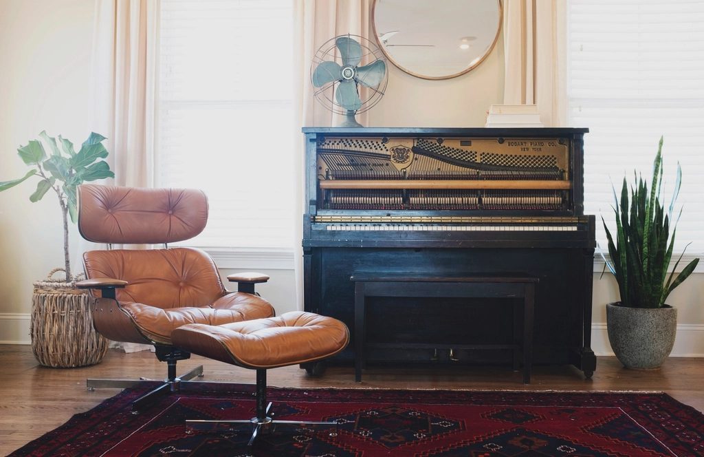 An upright piano in a bright living room beside a leather lounge chair